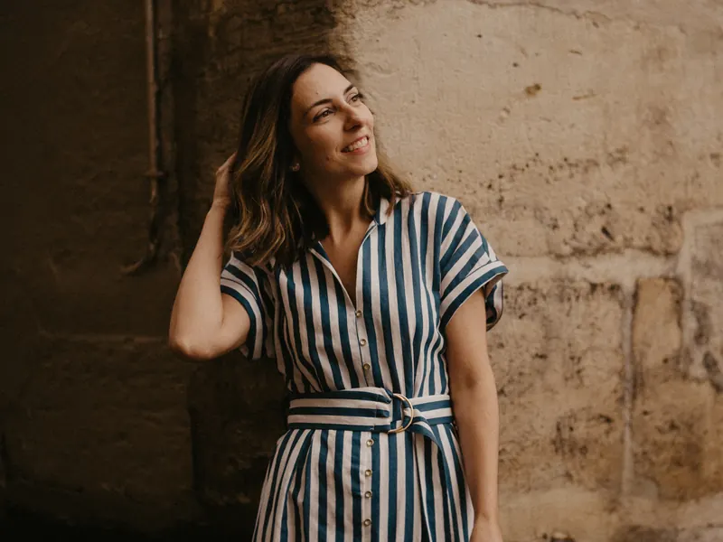 Mel Rolan sorrindo junto a um muro de pedra em Paris