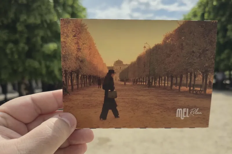 Cartão-postal com uma cena de filme, segurado na mesma alameda do Jardin des Tuileries onde ela foi gravada